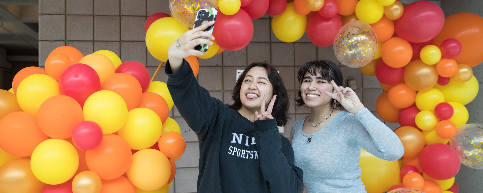 students taking a selfie in front of a balloon arch