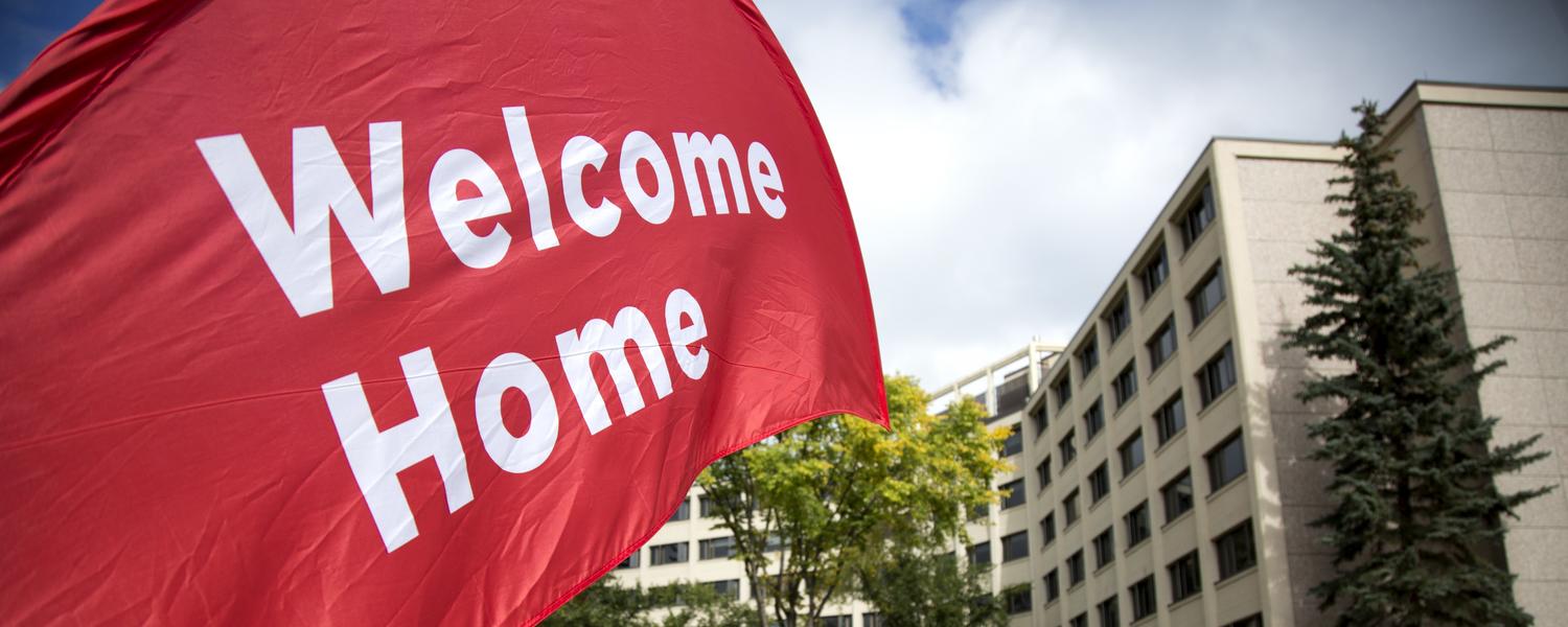 A flag in front of residence that reads "Welcome Home".