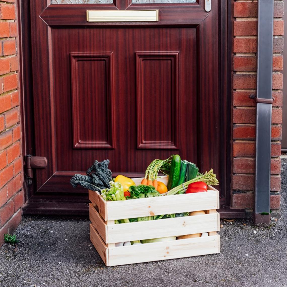wooden crate with vegetables in it sitting on pavement in front of dark wooden door