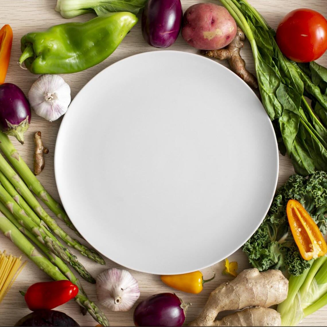 Top down image of empty white dinner plate surrounded by fresh vegetables