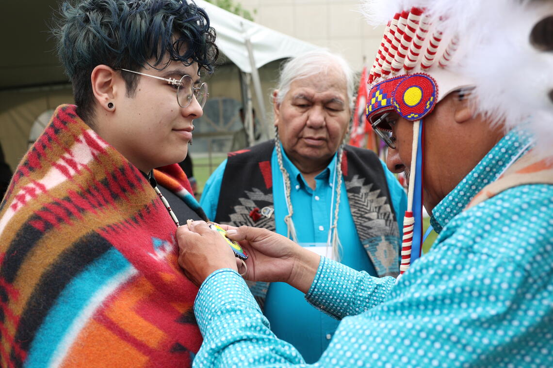 A student receiving a medallion from an Elder.
