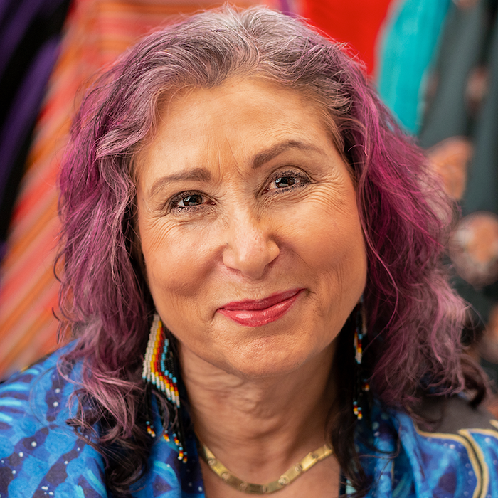 A woman with purple hair smiles at the camera