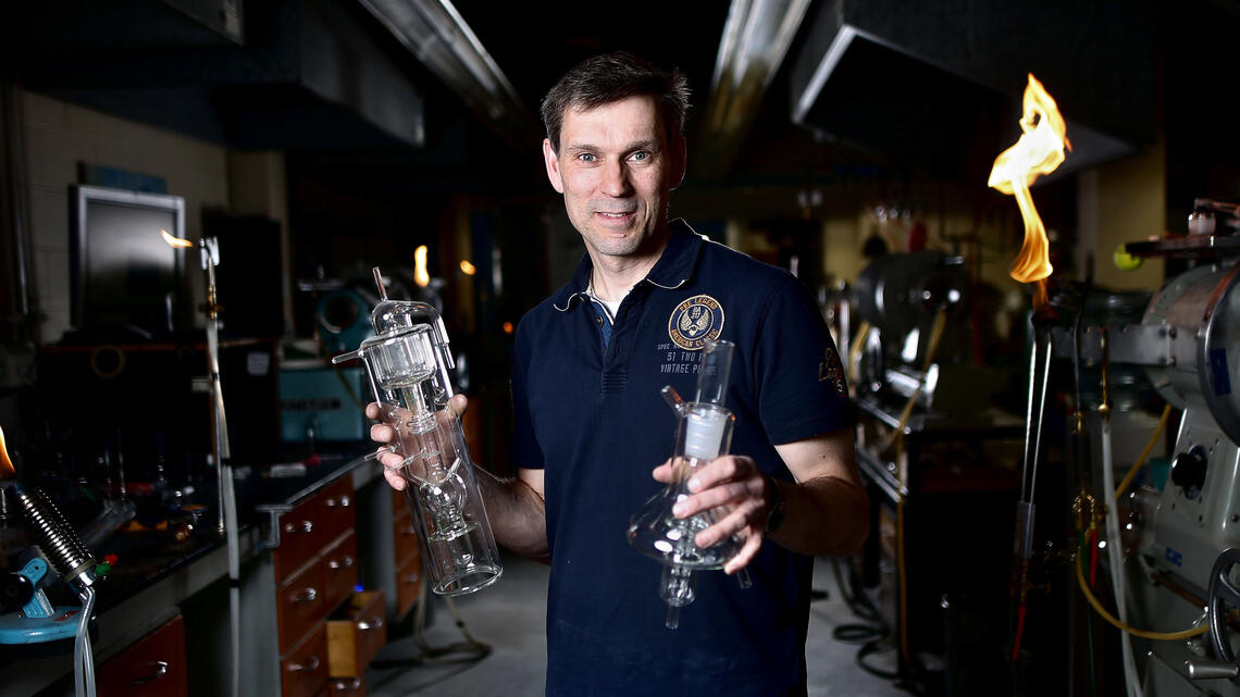 A man holds two glass bottles in front of machinery and saved