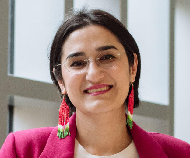 A woman with short dark hair, glasses and beaded earrings smiles at the camera