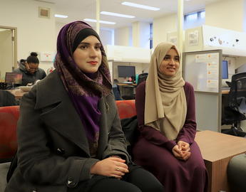 two women wearing hijab sit on a couch
