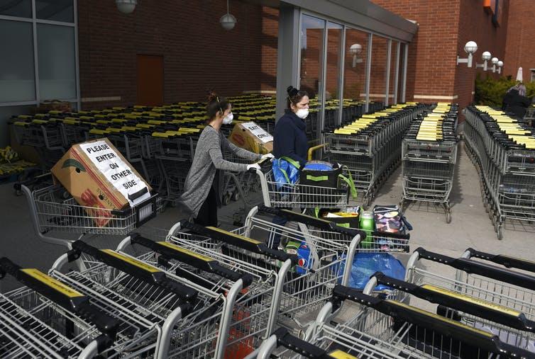 People leave a grocery store in Ottawa where carts and signs have been placed to facilitate physical distancing in response to the COVID-19 pandemic on April 4, 2020.
