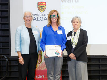 Dr. Cari Din (Faculty of Kinesiology), centre, receives the McCaig-Killam Teaching Award from Killam Trustee Brendan Eaton, left, and Interim Provost Penny Werthner, right