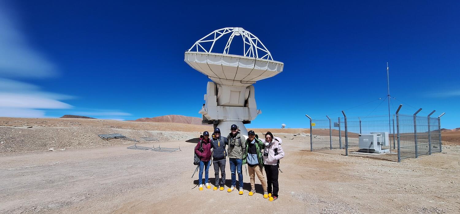 The team standing in front of a Telescope at ALMA.