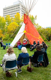 Students and staff sit in a circle around the UCalgary tipi