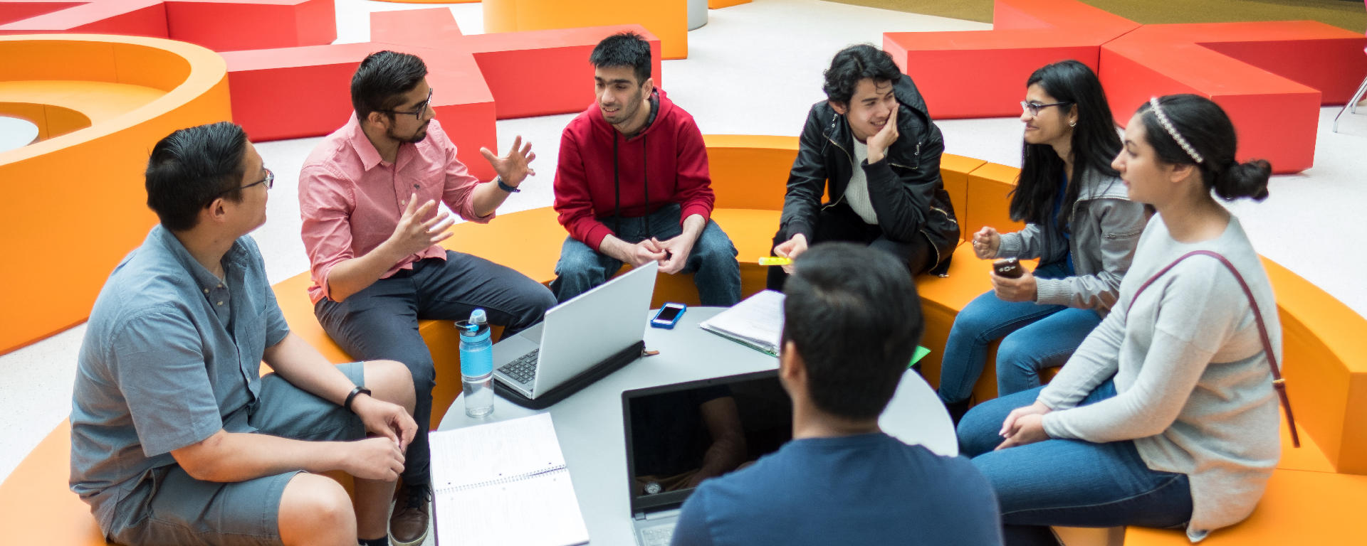 Students sitting in a circle with laptops and notebooks, talking to each other.