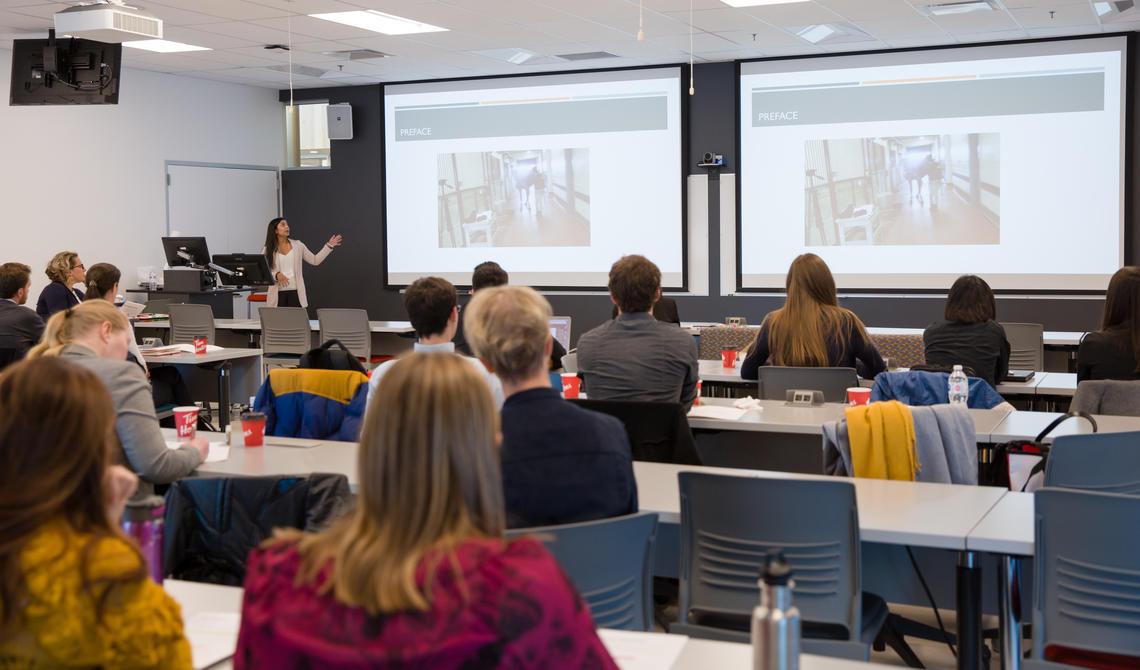 Students sitting in a classroom looking at two presentation screeens.