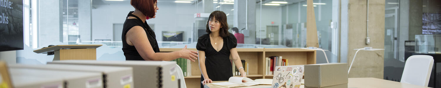 A student and supervisor in conversation in a library.