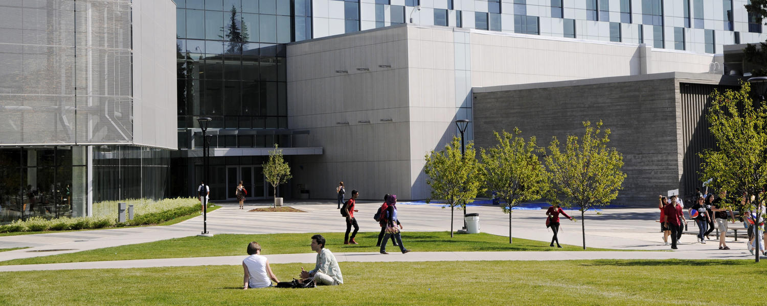 Image of two students sitting on the grass outside UCalgary TFDL Library