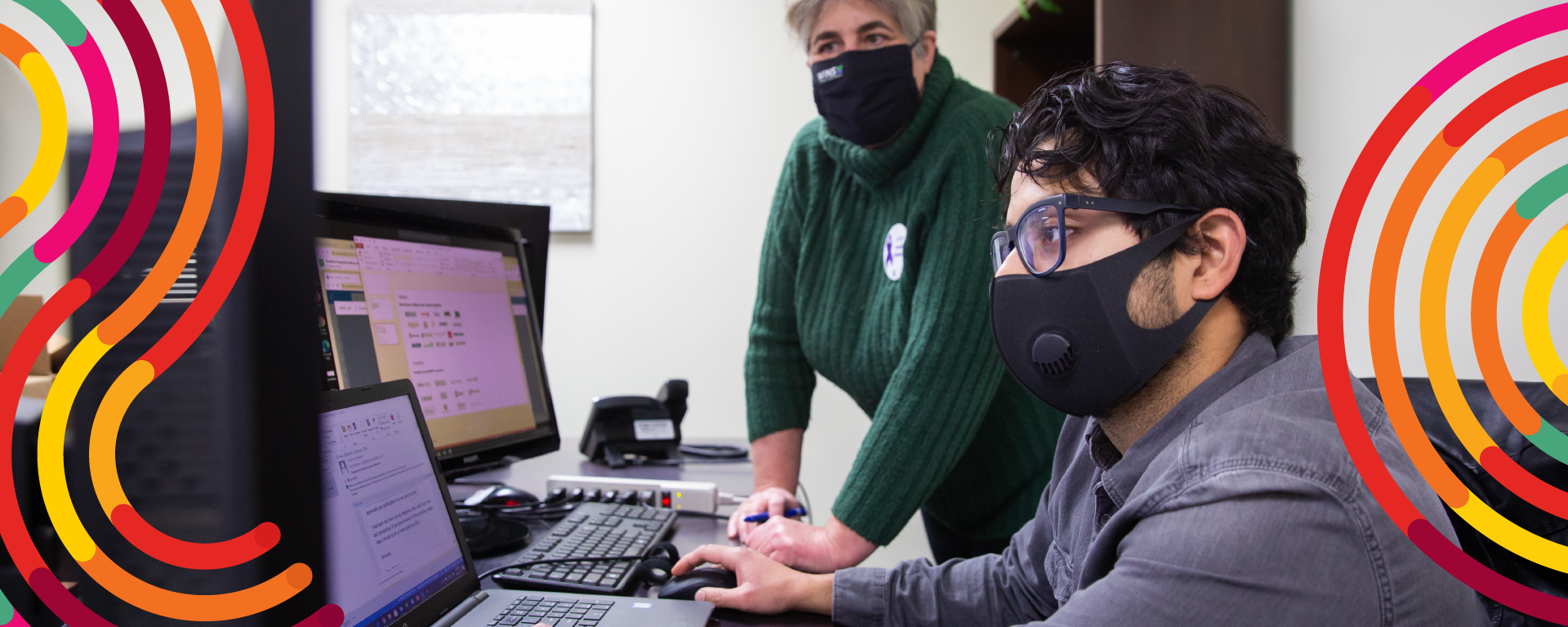 Student working on a computer with multiple screens, a supervisor is standing beside them