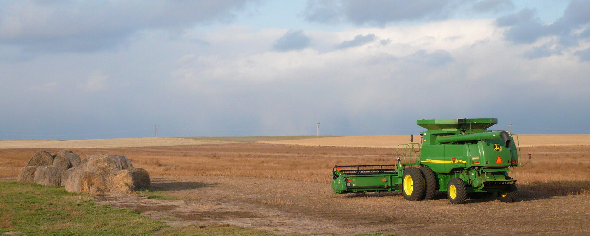 green combine in open field moving towards blue sky horizon