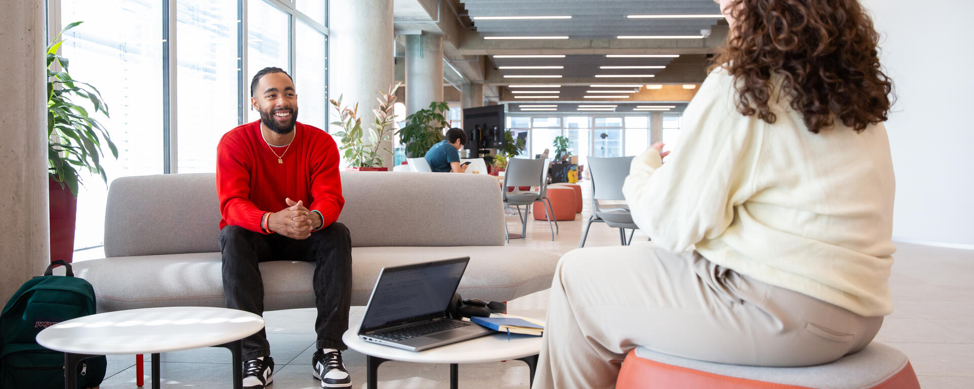 First-generation student Mikel Desjardins sits on a couch in the Hunter Student Commons, speaking with a female peer.
