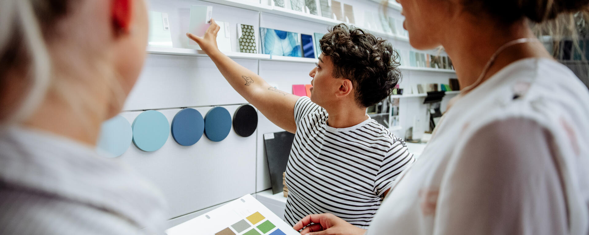 Someone is reaching for a sample of glass on a display while two other people stand beside them watching.