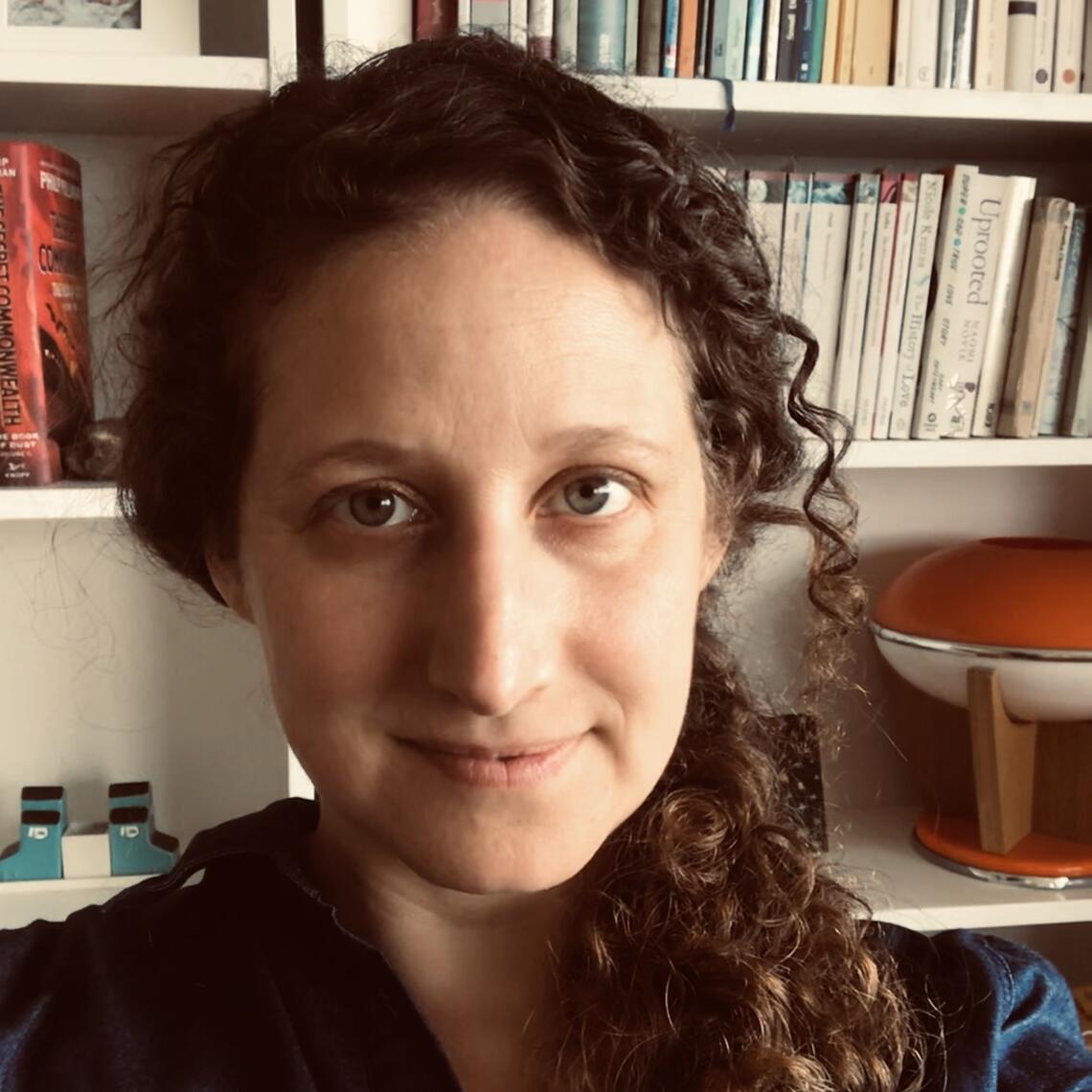 woman with long curly brown hair standing in front of bookshelf