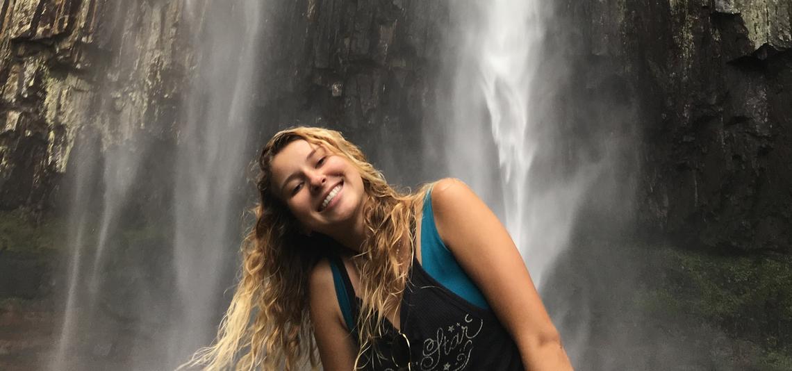 Long haired femme presenting student standing under a waterfall