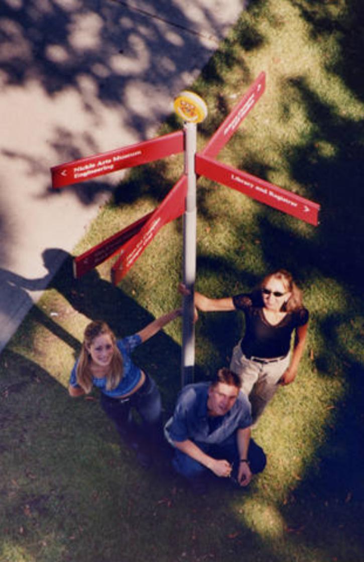 Students outdoors near a campus sign post, 2000.