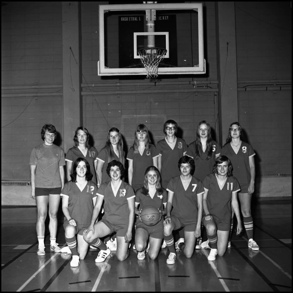 The University of Calgary Dinosaurs women's basketball team posing as a group in front of a basketball hoop.