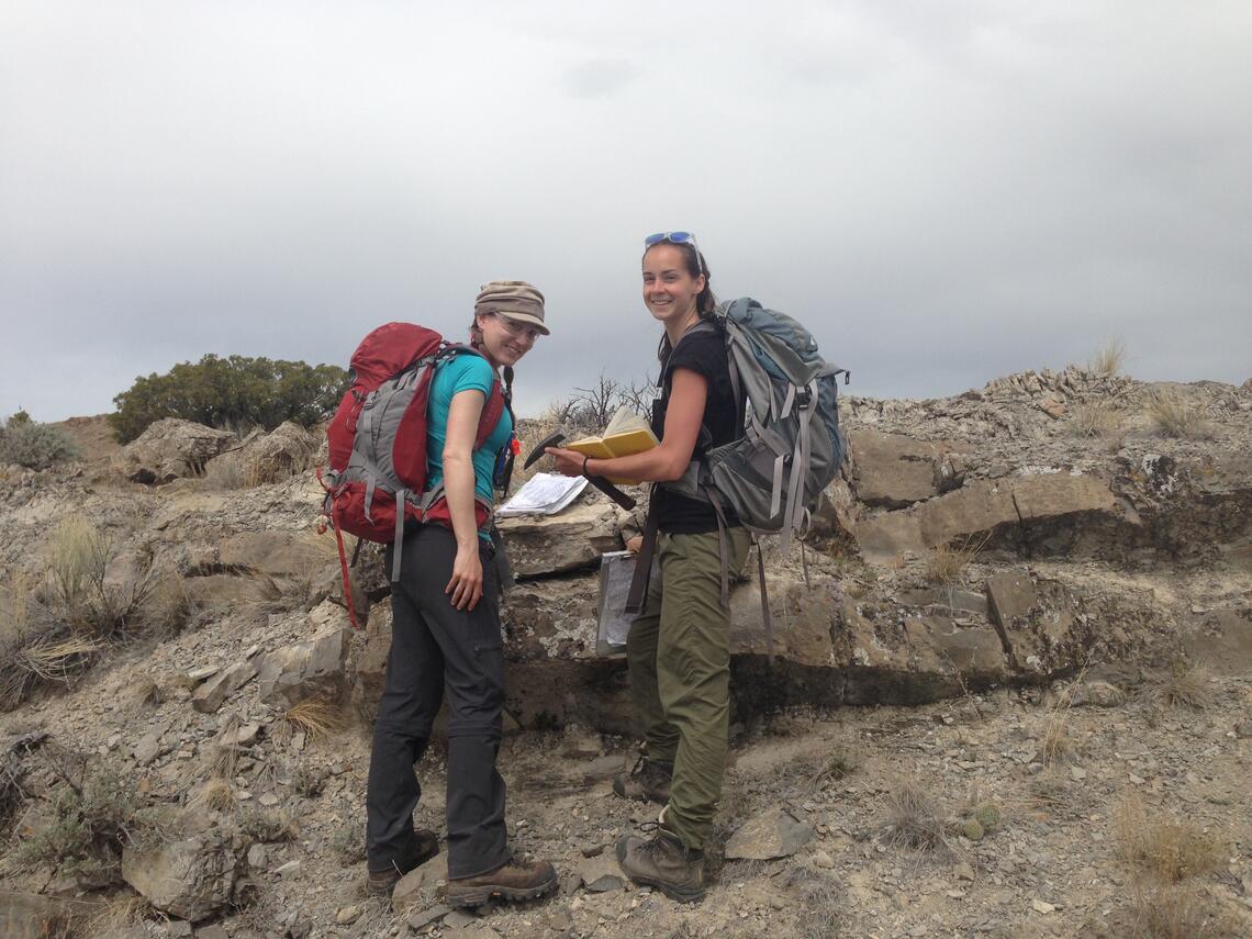 2 students holding notebooks beside rocky outcrop
