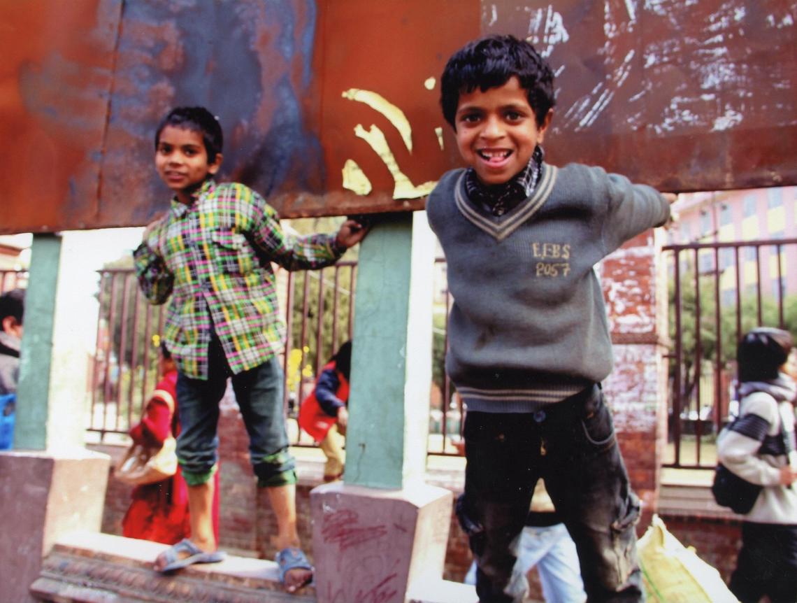 Two young children smiling while standing on a colourful stone wall