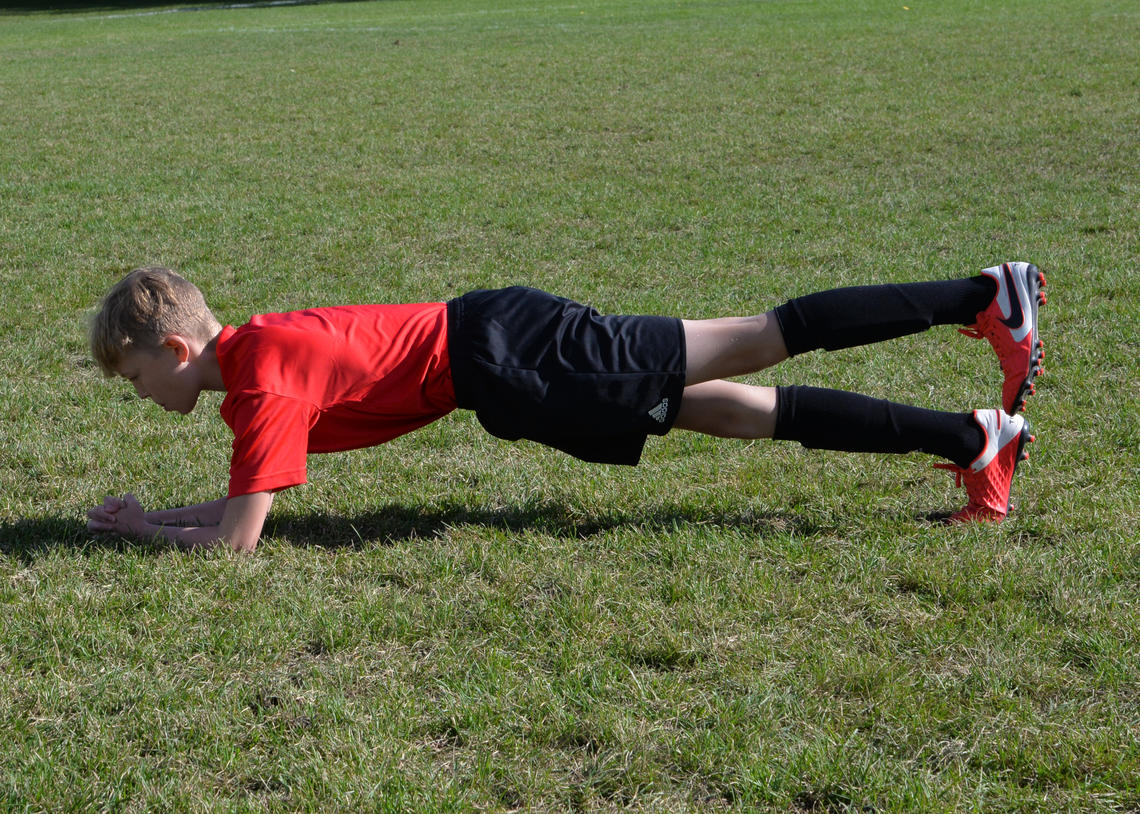 Soccer player performing front plank with leg lifts