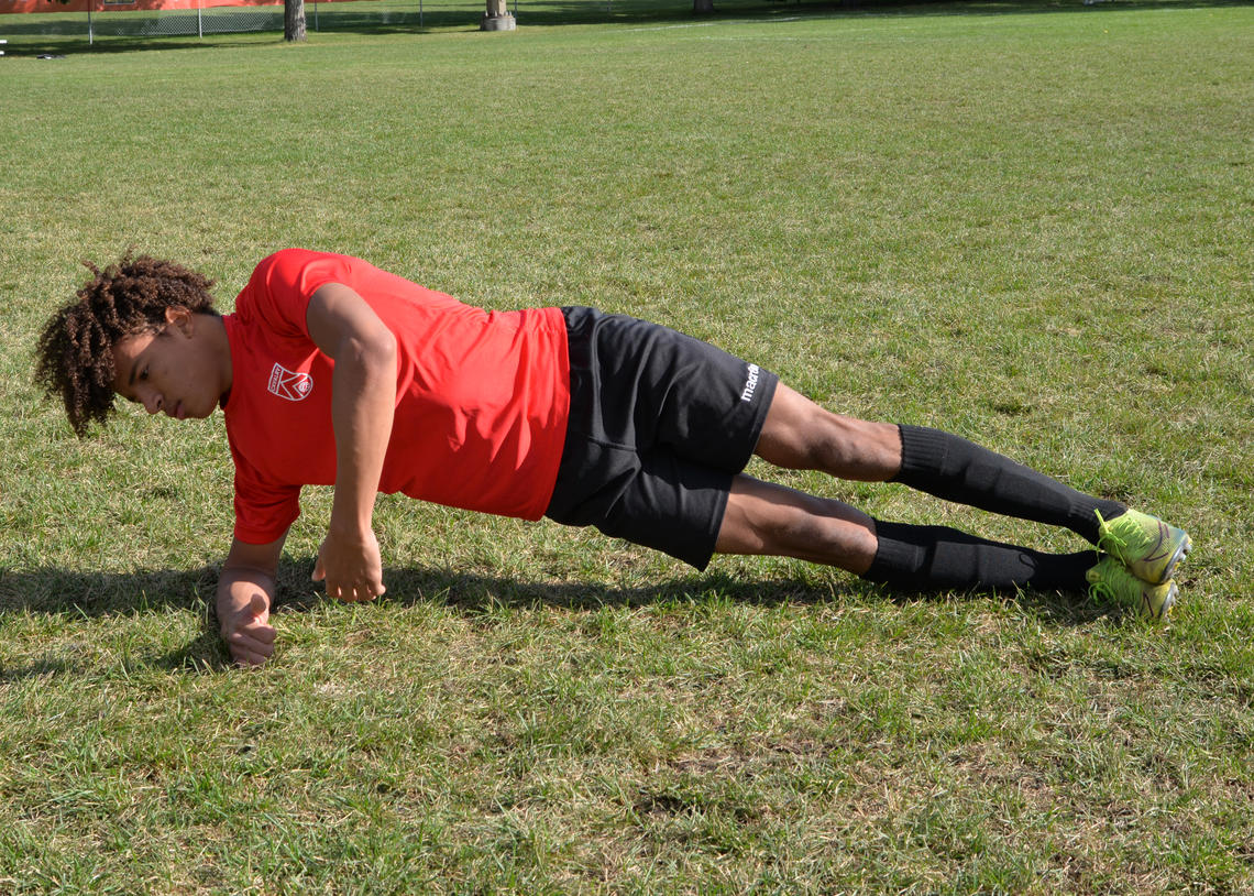 Soccer player performing side plank with torso rotations