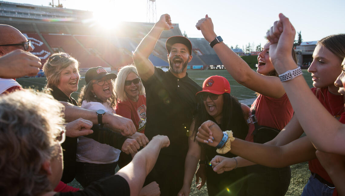 Chancellor Jon Cornish and other community members gathered on the football field, raising their hands in celebration.