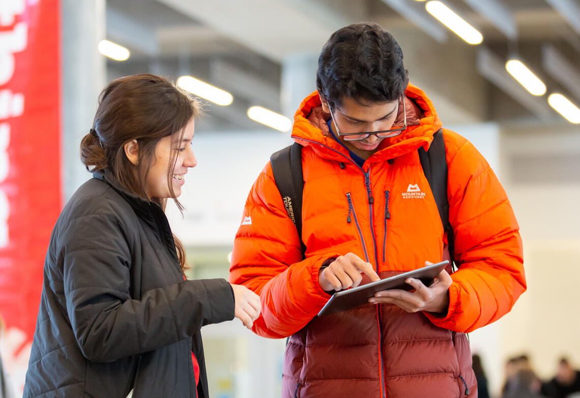Two people standing in the Hunter Student Commons, talking and interacting with an iPad.