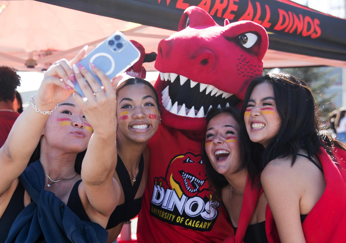 Four UCalgary students pose for a selfie photo with the Dinos mascot
