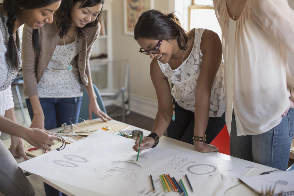 Young workers gather around a table with drawings on it.