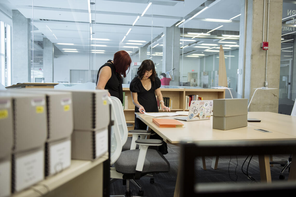 A student and supervisor look at documents in the library.