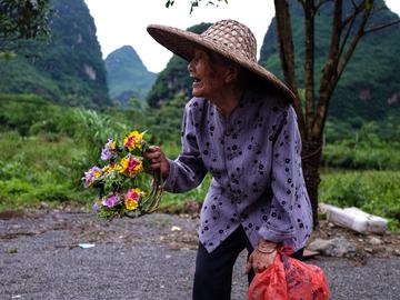 Image of a woman with straw hat holding flowers at roadside