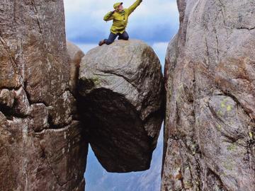 Image of a man balanced high above a fjord while rock climbing
