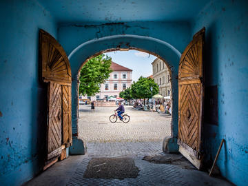 Image looking out through blue doorway as a woman rides past on a bicycle