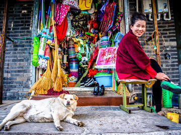 Image of a shopkeeper with colourful blankets and a dog lying beside
