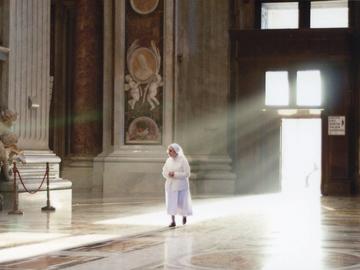 Image of a white robed woman walking through doorway with sunlight behind her