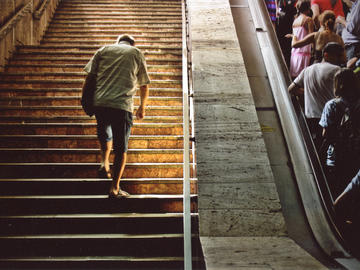 Image of man walking up wooden stairs while a crowd of people rides an escalator beside him