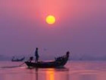 A fluorescent sun against a pink and purple sky. A river reflecting those very colours. A boat with two silhouetted figures are centred on the photo