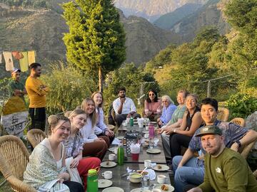 Students sitting around an outdoor dinner table with mountain & Tibetan prayer flags in background