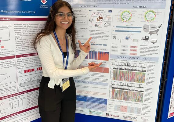 Undergraduate student at a conference with a research poster behind them.