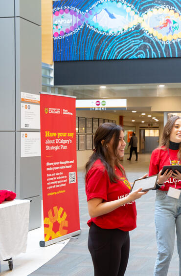 Two students in a lobby encouraging passersby to have their say about UCalgary's strategic plan
