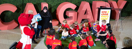 Group of kids sitting in front of a woman reading from a story book