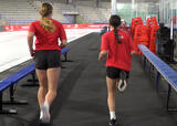Two athletes performing butt kicks exercise near a hockey rink