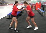 Athletes performing a partner stick wrestle exercise in an ice hockey arena