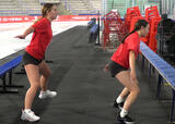 Two athletes performing side shuffles with arm swings exercise near a hockey rink