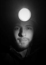 A young bearded man wearing a miner's headlamp