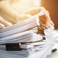 A stack of papers on a desk, some with butterfly clips on them, with someone picking up the top few pages